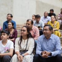 Parents and students sitting together on outdoor amphitheater steps watching a school performance.