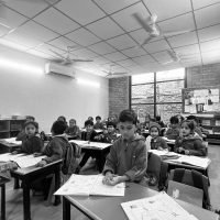 Black and white image of students sitting at wooden desks in a bright classroom.