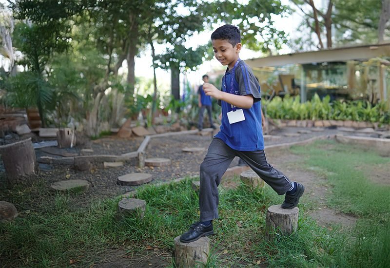 Young Student Stepping Across Log Balance Posts Outdoors